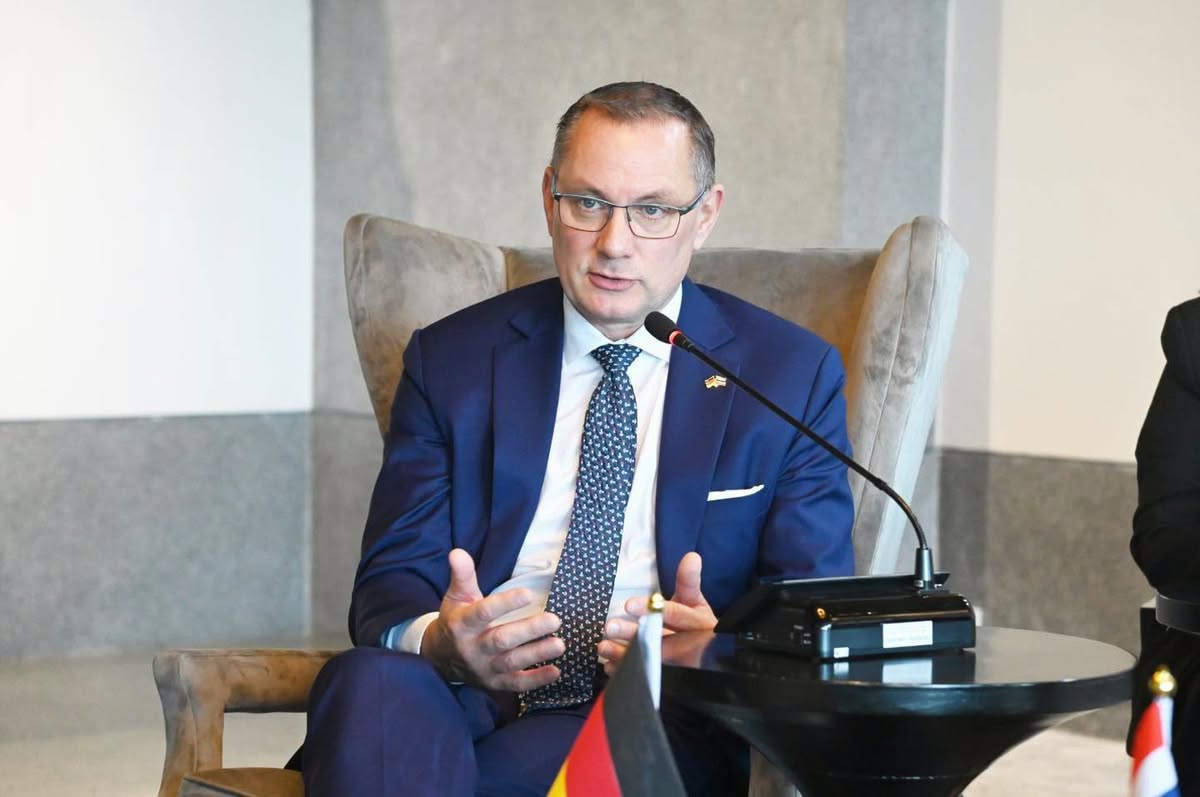 Mann im blauen Anzug mit Brille spricht in ein Mikrofon, im Vordergrund eine deutsche Flagge